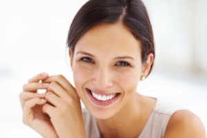 Smiling woman with dark hair pulled back holding her hands near her face against a bright background