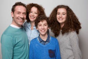 Smiling family of four posing closely together against a plain grey background